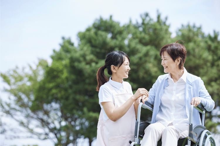 病院の庭で車椅子の女性の手をとる介護士
